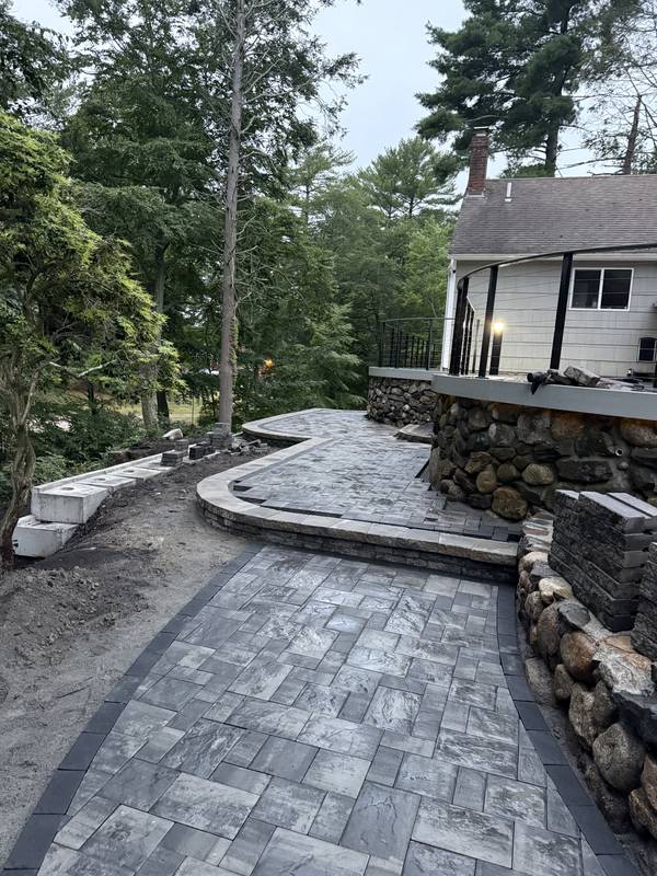 Paver walkway flowing past the stone retaining wall to the house